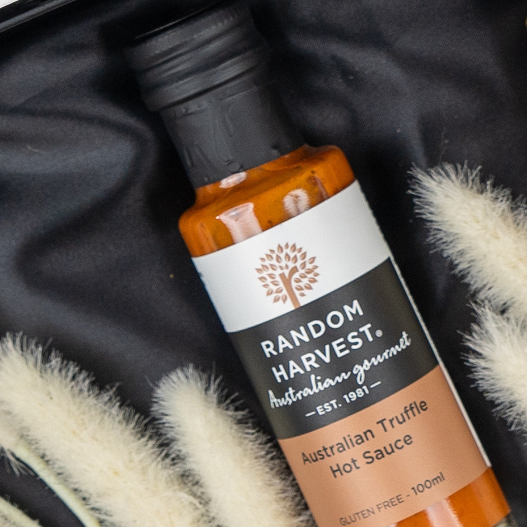 A box of The Hamper Boutique Co's Macallan Indulgence Hamper rests on black fabric near beige dried grasses. The hamper’s label is visible, displaying the brand and its premium presentation.
