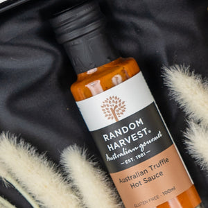 A box of The Hamper Boutique Co's Macallan Indulgence Hamper rests on black fabric near beige dried grasses. The hamper’s label is visible, displaying the brand and its premium presentation.