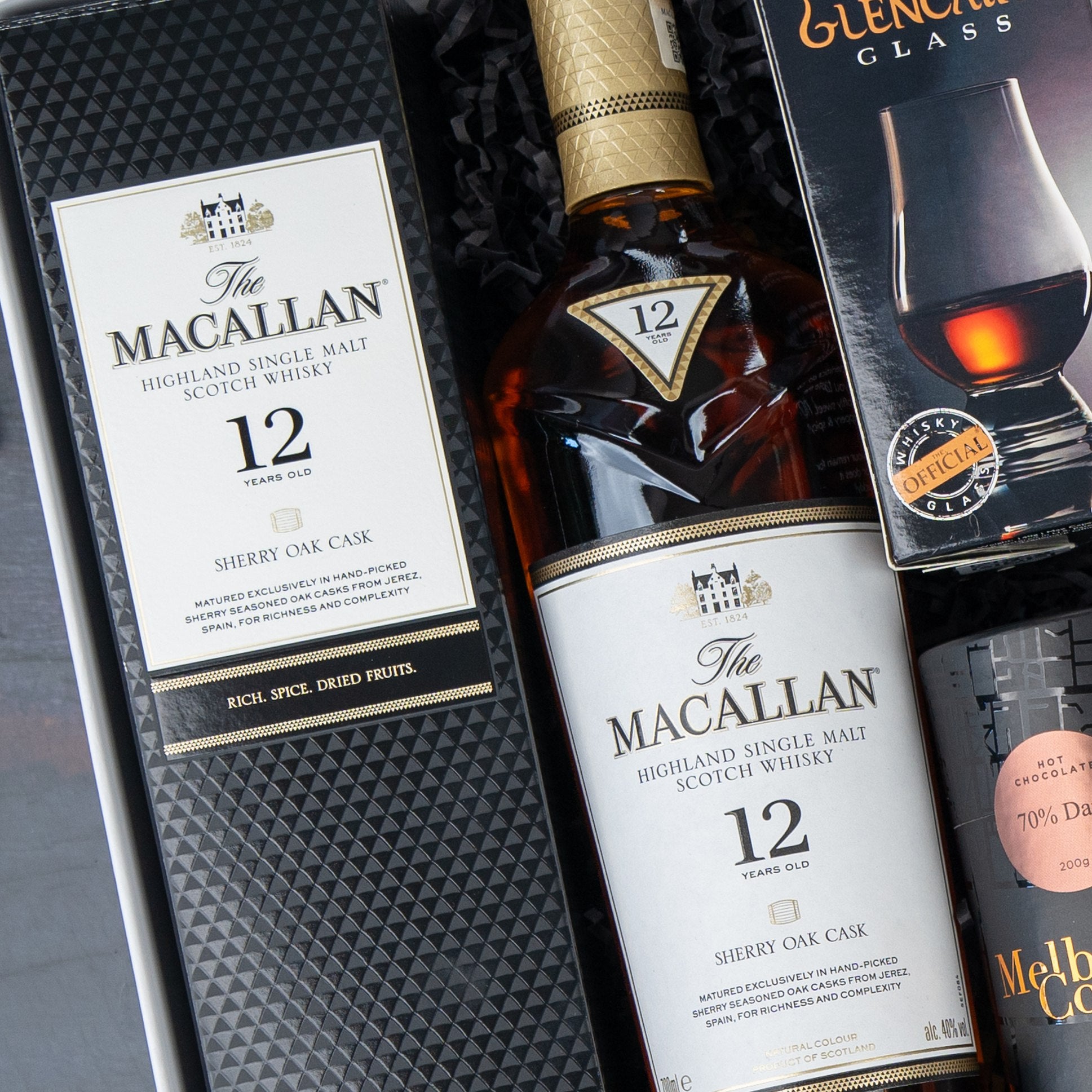 The Hamper Boutique Co's Macallan Collector's Edition Hamper includes a bottle of The Macallan 12 Year Old Highland Single Malt Scotch Whisky, its box, a Glencairn glass box, and a Meltdown dark chocolate bar.