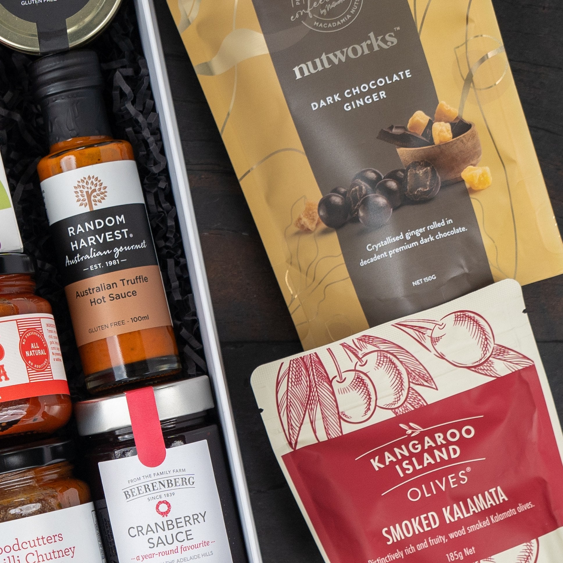 The Hamper Boutique Co's Macallan Collector's Edition Hamper features gourmet sauces, chutney, cranberry sauce, dark chocolate ginger, and smoked kalamata olives—all elegantly arranged on a dark surface.