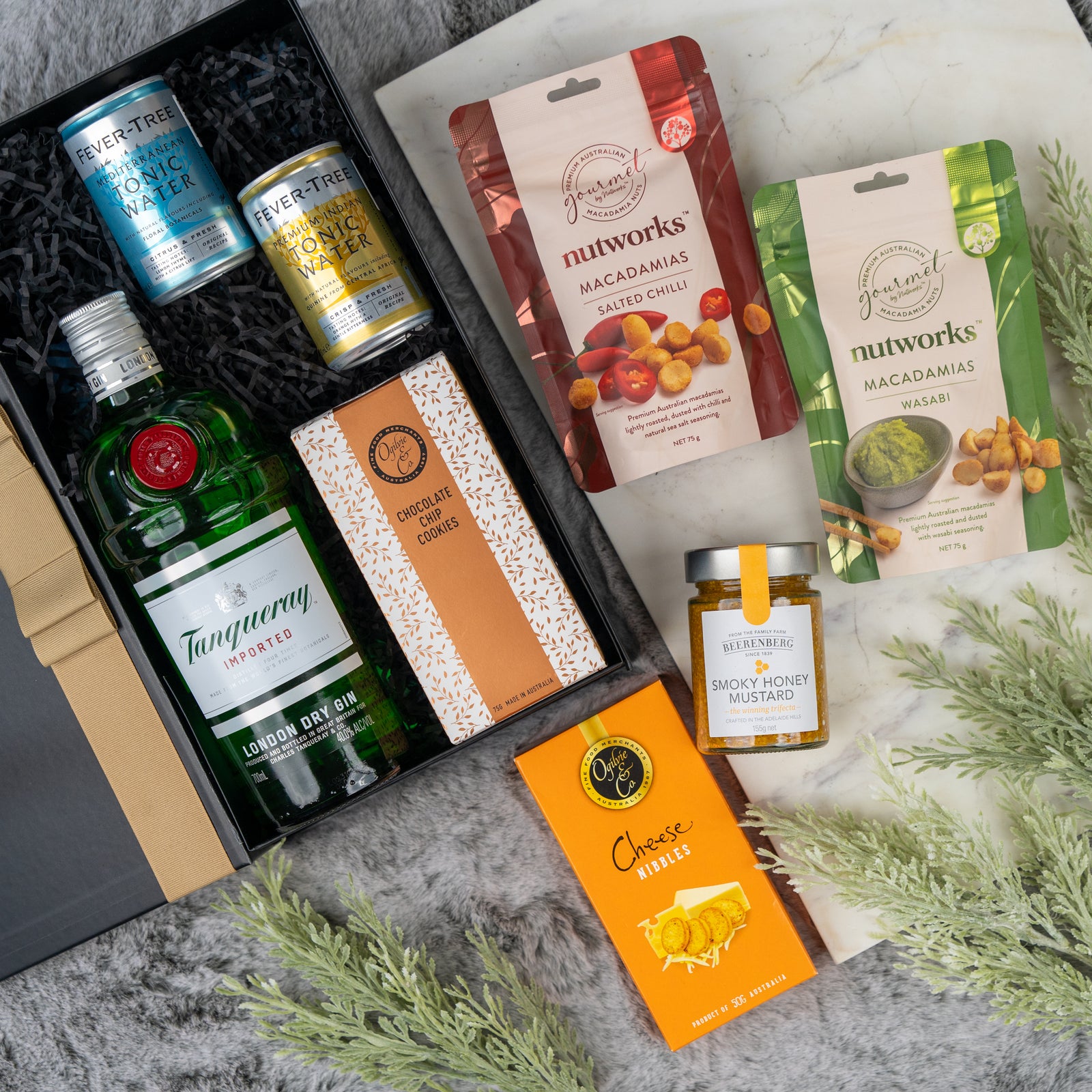 The Tanqueray Gin Journey Hamper by The Hamper Boutique Co features Tanqueray gin, Fever-Tree tonic cans, chocolate, cheese bites, honey mustard, and two Nutworks macadamia packs in a beautifully arranged gift box.