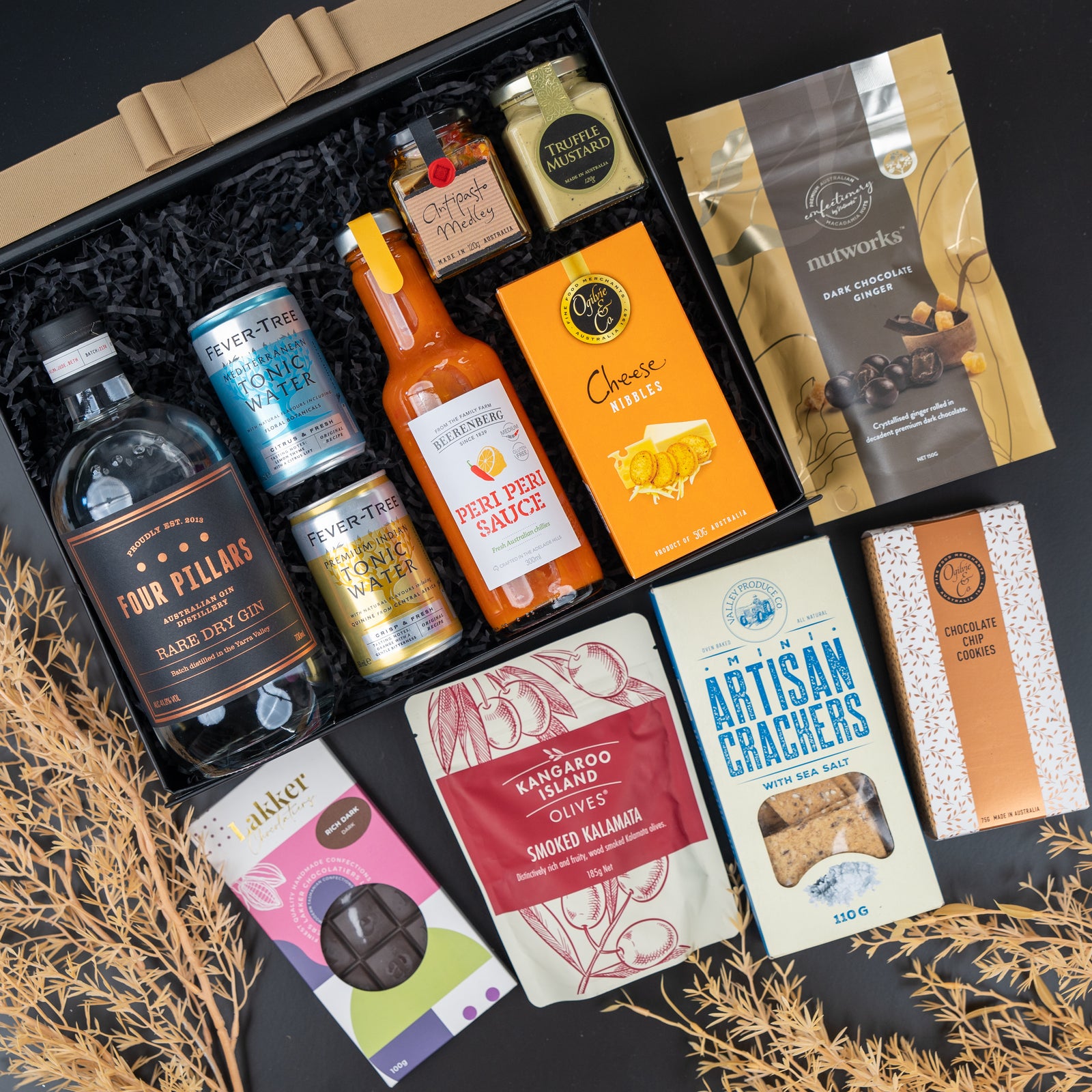 The Hamper Boutique Co's Four Pillars Signature Collection Hamper features gin, tonic water, hot sauce, jam, dark chocolate, cheese nibbles, crackers, olives, chocolate cookies and choc-covered almonds in a neatly arranged gift box.