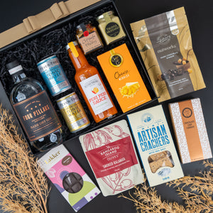 The Hamper Boutique Co's Four Pillars Signature Collection Hamper features gin, tonic water, hot sauce, jam, dark chocolate, cheese nibbles, crackers, olives, chocolate cookies and choc-covered almonds in a neatly arranged gift box.