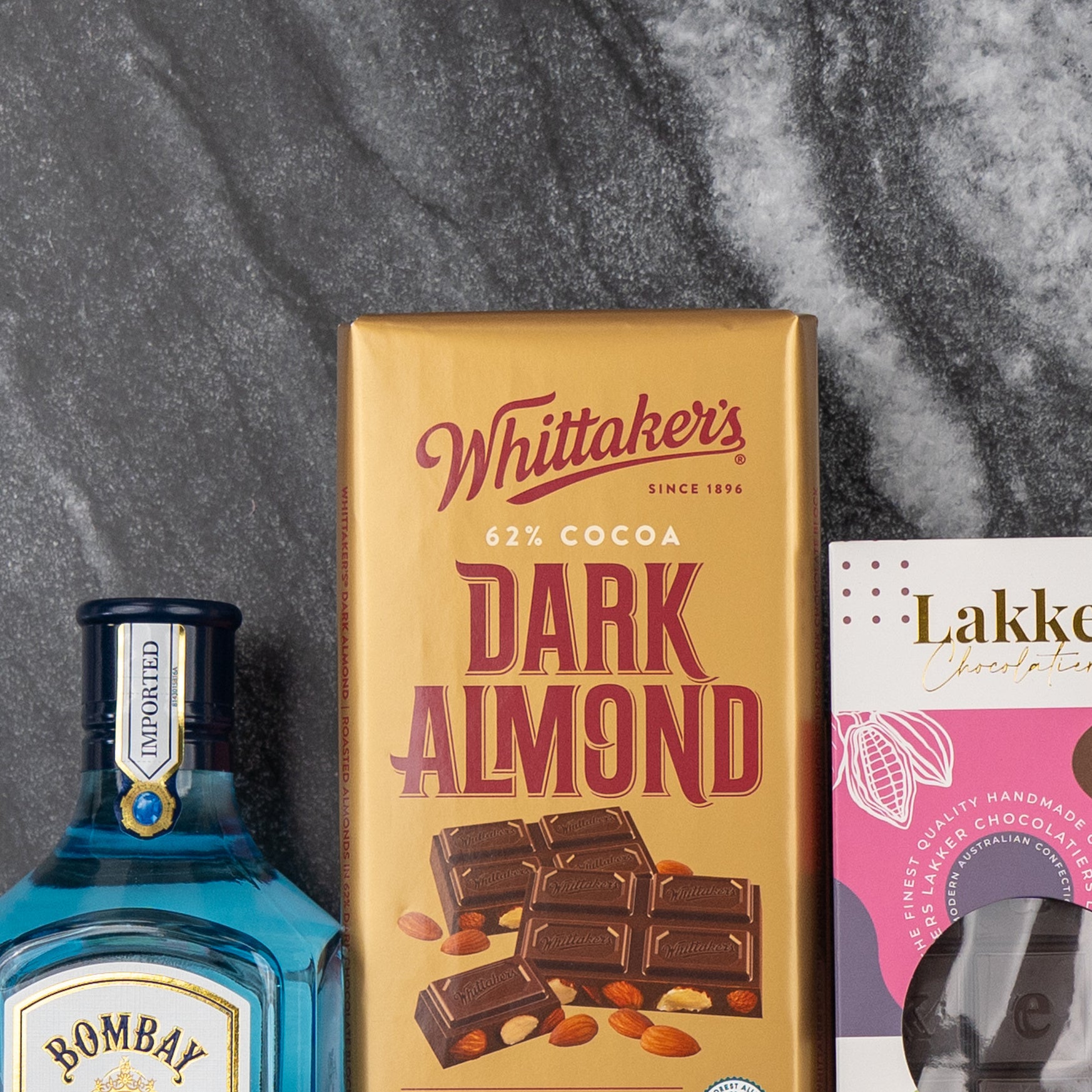 The Hamper Boutique Co's Bombay Sapphire Indulgence Hamper, featuring premium gin and exquisite chocolates, is elegantly arranged on a dark marble surface.