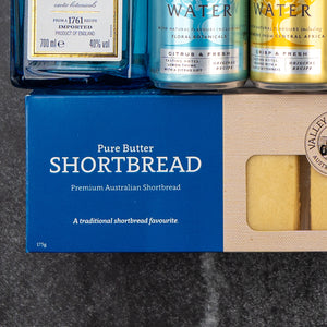 The Hamper Boutique Co's Bombay Sapphire Indulgence Hamper features a box of Premium Australian Shortbread with two biscuits visible beside tonic water and a gin bottle, all arranged on a dark surface.