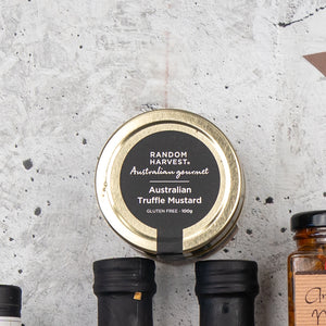A top view of a jar labeled Four Pillars Premium Gin Hamper by The Hamper Boutique Co with a gold lid, placed on a textured gray surface next to bottles with black caps.