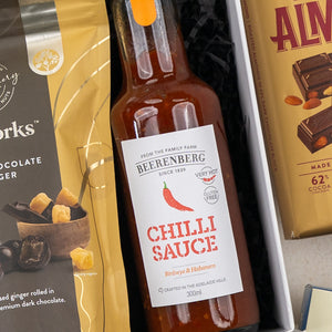 A Four Pillars Botanical Discovery Hamper from The Hamper Boutique Co is placed between a bag of dark chocolate ginger bites and a bar of almond chocolate. Its label highlights botanical elements and gifting appeal.