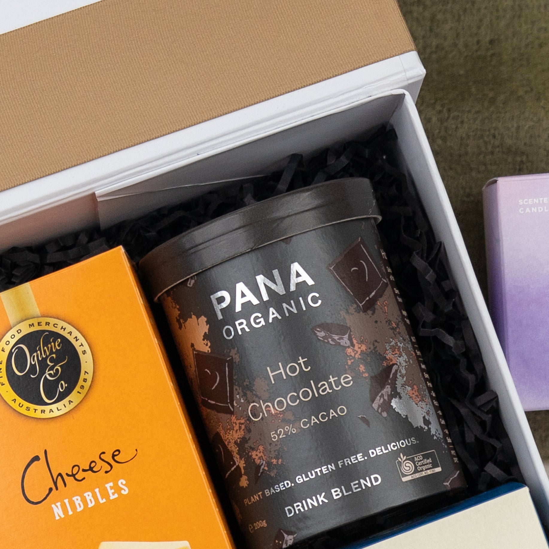 The Hamper Boutique Co Four Pillars Ultimate Gin Experience Hamper features a selection of treats and gifts, all elegantly presented in black shredded paper.