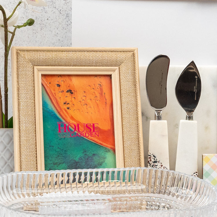 The Homeware Bliss Gift Hamper by The Hamper Boutique Co features a framed beach print, two white-handled cheese knives, and a clear glass tray.