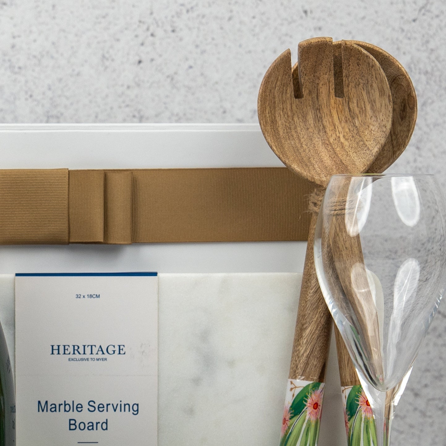 The Hamper Boutique Co’s Ultimate Celebration Hamper includes a marble serving board with brown ribbon, two wooden salad servers, a clear wine glass, and a Heritage Marble Serving Board card set against a light textured background.