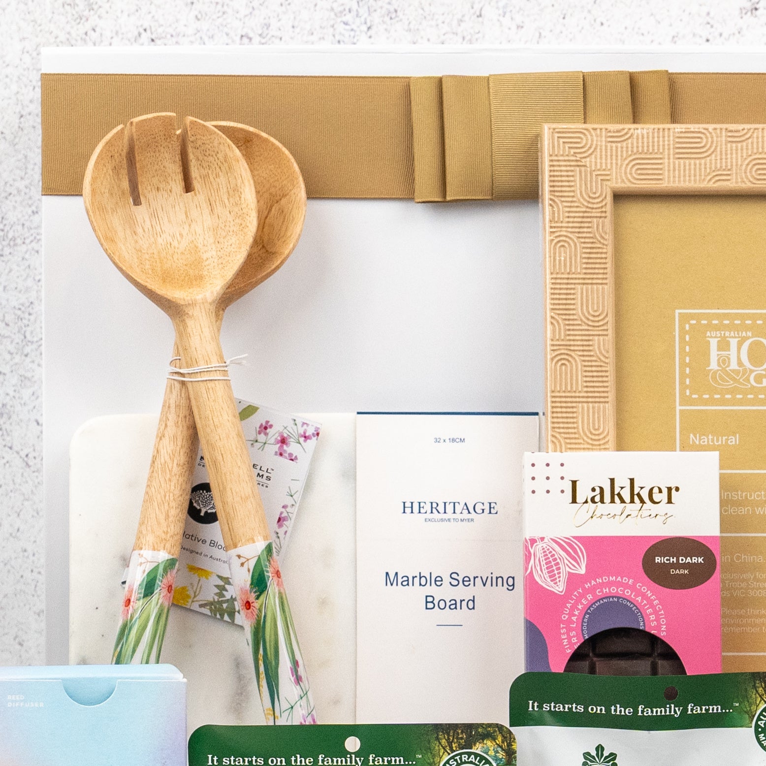 A close-up of The Hamper Boutique Co’s Wellness and Homeware Hamper, featuring wooden salad servers, a marble serving board, a wooden frame, and gourmet chocolate, all beautifully packaged.