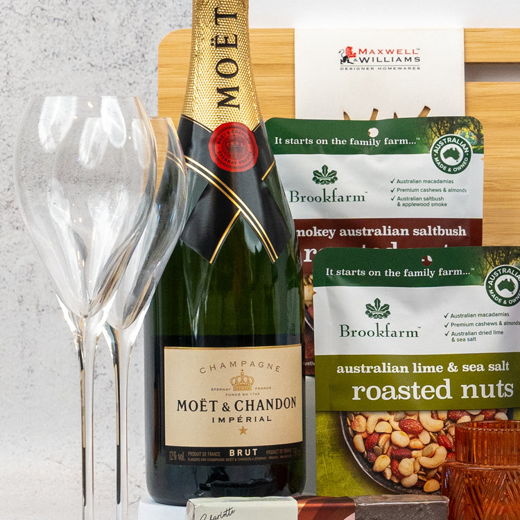 The Hamper Boutique Co's Ultimate Homeware Gift Hamper features Moët & Chandon champagne, two wine glasses, Brookfarm snacks, and a wooden cheese board, curated for a gourmet gifting experience.