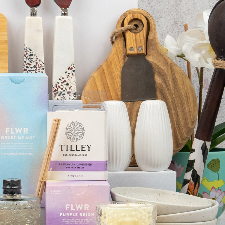 The Hamper Boutique Co's Ultimate Homeware Gift Hamper features chopping boards, salt and pepper shakers, bowls, a candle, reed diffuser, boxed soaps, utensils, and white artificial orchids arranged beautifully together.