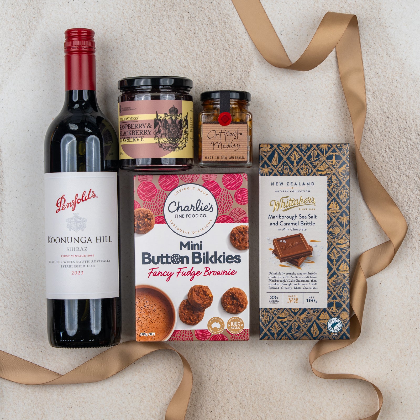 The Hamper Boutique Co's Taste Explorer Gift Hamper features Penfolds Kooyong Hill Shiraz, raspberry jam, chutney, mini fudge brownie biscuits, and Whittakers chocolate, beautifully arranged with a gold ribbon.