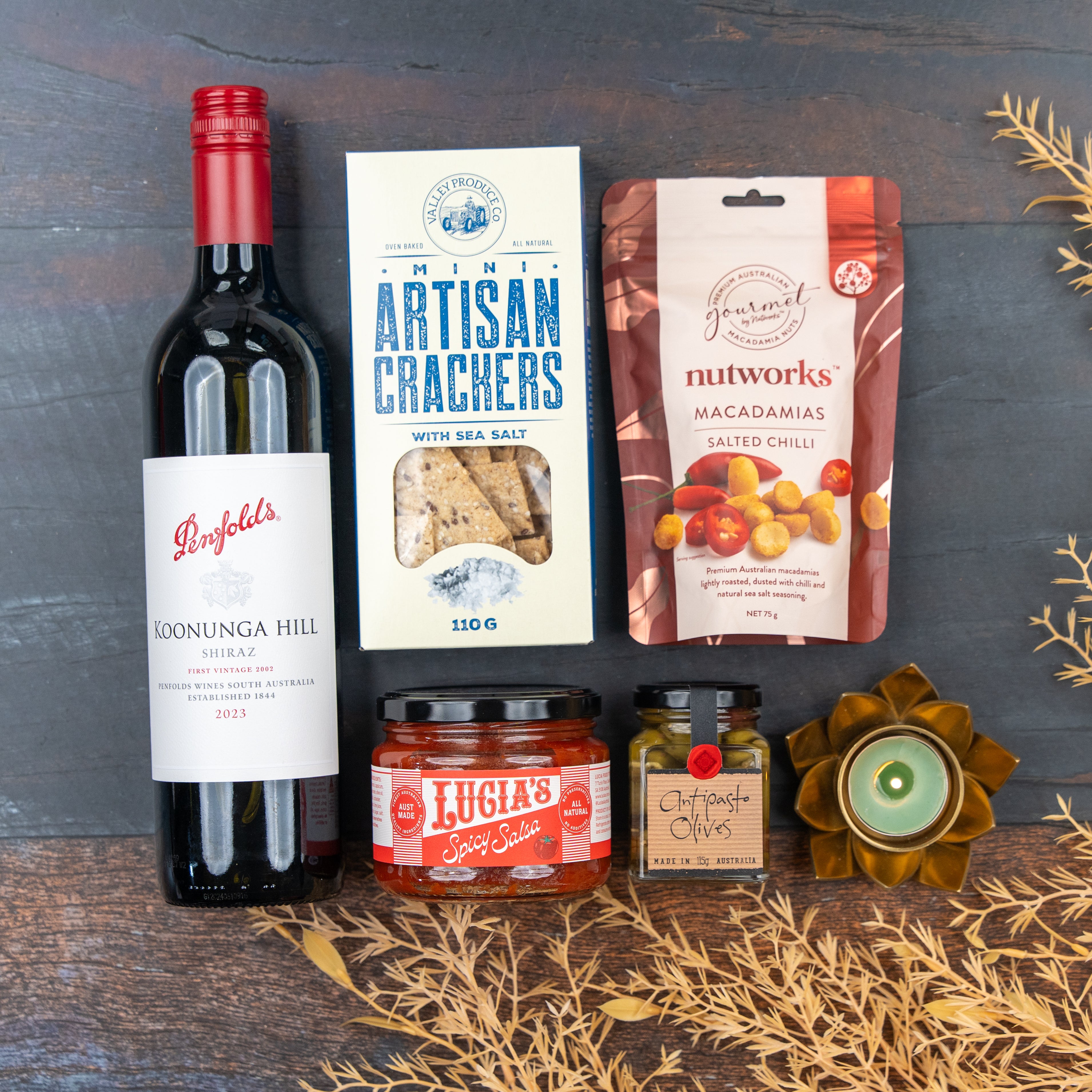 The Hamper Boutique Co Savoury Selection Gift Hamper includes Penfolds Koonunga Hill Shiraz, artisan crackers, salted chili macadamias, Lucias Spicy Salsa, antipasto olives, and a decorative tealight on a gold-accented display.