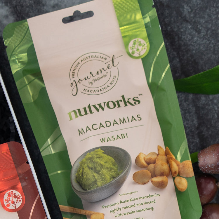 A Flavour Fiesta Gift Hamper by The Hamper Boutique Co, featuring green and beige packaging with leafy accents and images of macadamia nuts and a bowl of green wasabi paste on the front.