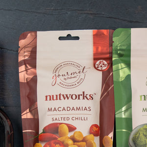 A close-up of The Hamper Boutique Co Festive Treats Gift Hamper, with a package showing images of treats and festive elements against a dark background. Another partially visible hamper is on the right.