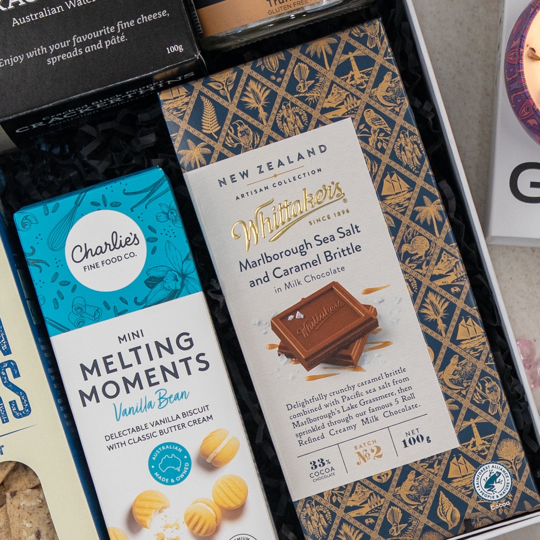 A close-up of The Hamper Boutique Co Deluxe Grazing Gift Hamper, featuring snacks like Whitaker’s Marlborough Sea Salt and Caramel Brittle milk chocolate, Charlies Mini Melting Moments vanilla bean biscuits, and more treats.