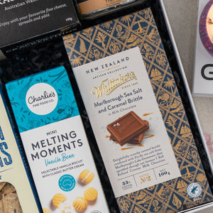 A close-up of The Hamper Boutique Co Deluxe Grazing Gift Hamper, featuring snacks like Whitaker’s Marlborough Sea Salt and Caramel Brittle milk chocolate, Charlies Mini Melting Moments vanilla bean biscuits, and more treats.