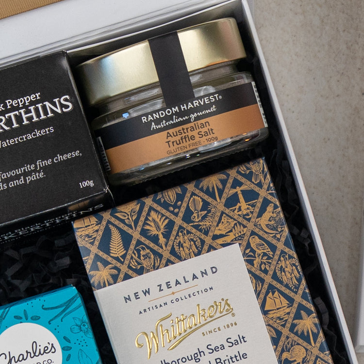 A close-up of The Hamper Boutique Co Deluxe Grazing Gift Hamper, featuring Australian truffle salt, gourmet pepper thins, and a Whittaker’s artisan sea salt & caramel brittle chocolate bar.