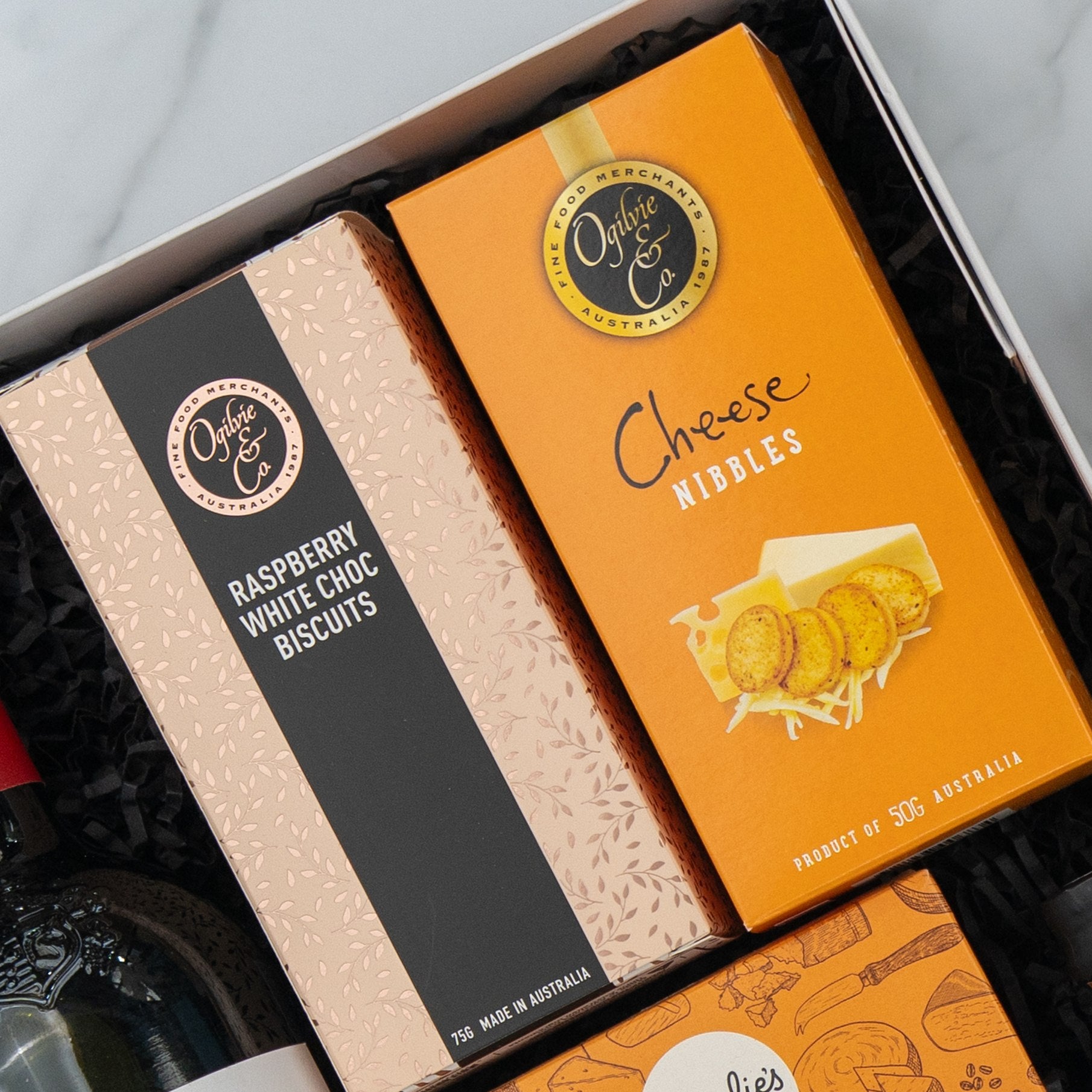 The Penfolds Celebration Hamper by The Hamper Boutique Co includes two gourmet snack boxes in a gift box: Raspberry White Choc Biscuits (pink box) and Cheese Nibbles (orange box).