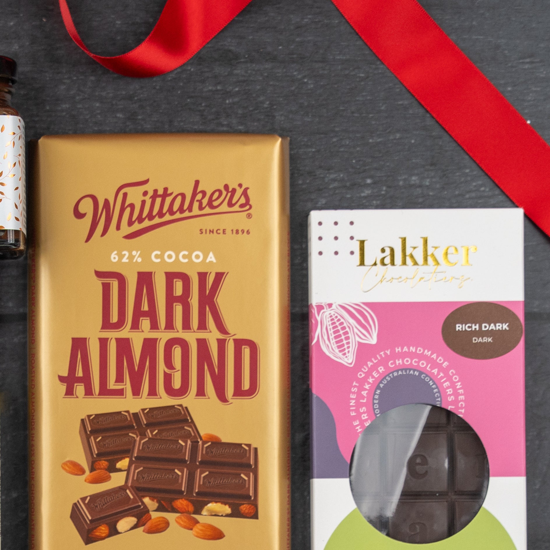 A Luxury Indulgence Gift Hamper from The Hamper Boutique Co is displayed on a dark surface beside a red ribbon.