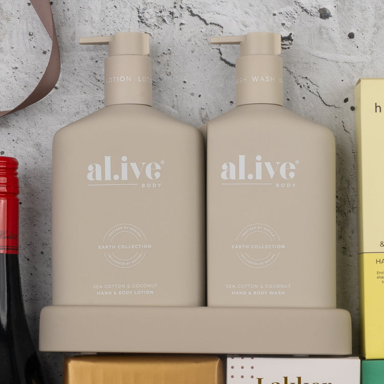 Two beige bottles from The Hamper Boutique Co’s Indulgent Evening Escape sit side by side in a matching tray—hand & body lotion on the left, hand & body wash on the right. Both bottles feature minimal text and a modern, neutral design.
