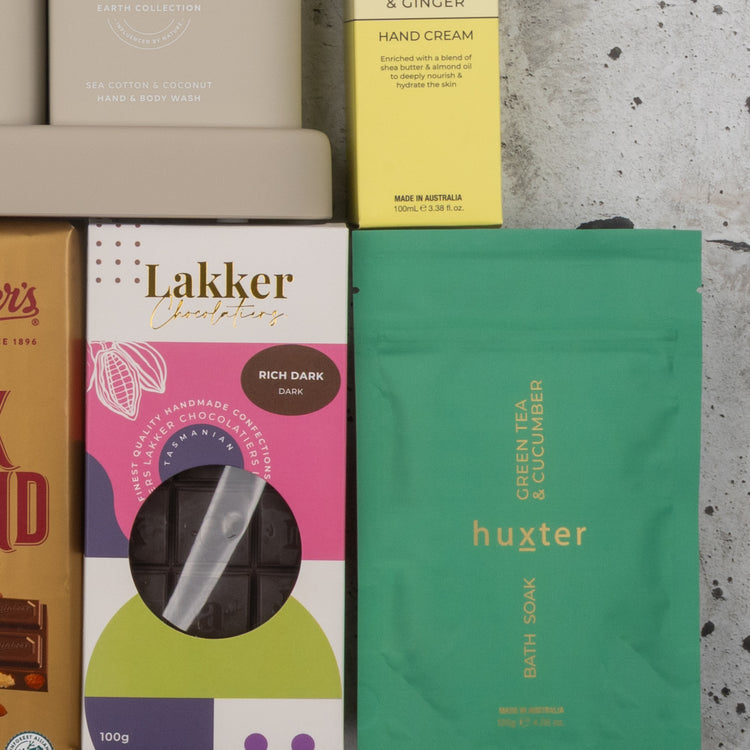 A flat lay of The Hamper Boutique Co’s Indulgent Evening Escape featuring hand cream, chocolate bars, a bath soak, and handmade chocolates arranged on a marble surface.