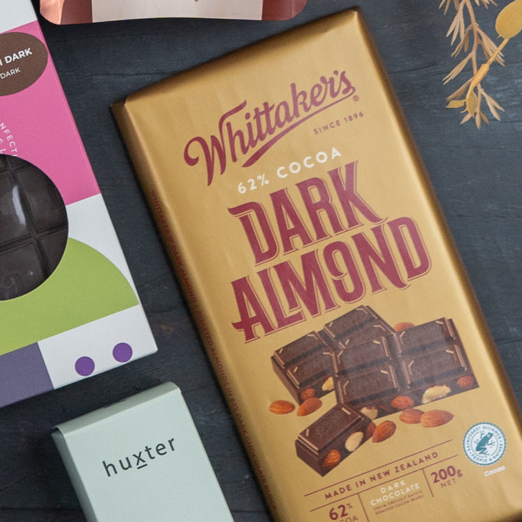 A Red Wine Culinary Experience Hamper from The Hamper Boutique Co is placed next to a pale green Huxter box, with partially visible chocolate and gift packaging on the surface.