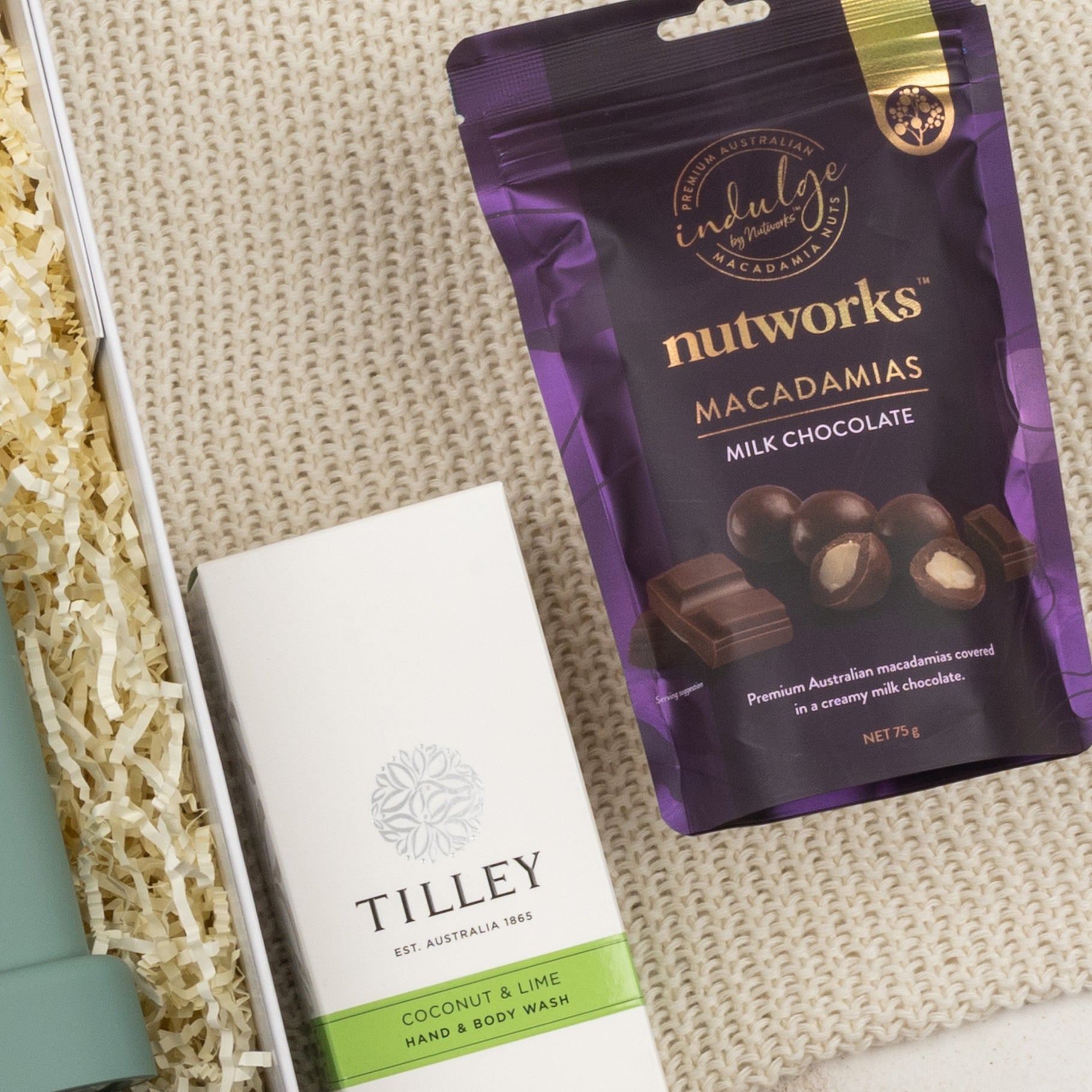 A flat lay of The Hamper Boutique Co's Relaxing Red Wine Hamper box, placed on a beige textured surface with shredded paper packaging beside it.
