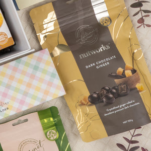 A close-up of The Hamper Boutique Co's Deluxe Wine and Relaxation Hamper, showcasing elegant items from the hamper, surrounded by pastel-toned packaging on a cream patterned surface.