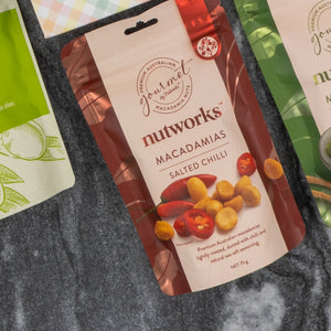 A Deluxe Wine and Relaxation Hamper by The Hamper Boutique Co rests on a gray surface, surrounded by other gift items. The elegant packaging features wine and relaxation products attractively displayed on the front.