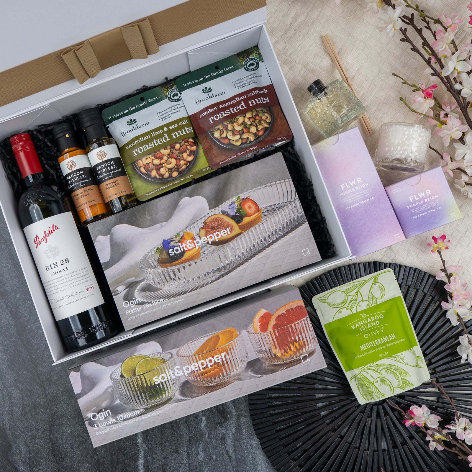 The Luxe Dining Red Wine Hamper by The Hamper Boutique Co includes Penfolds wine, gourmet nuts, olive oil, spices, a candle, and glassware, beautifully arranged with elegant decorative elements for the perfect gift.