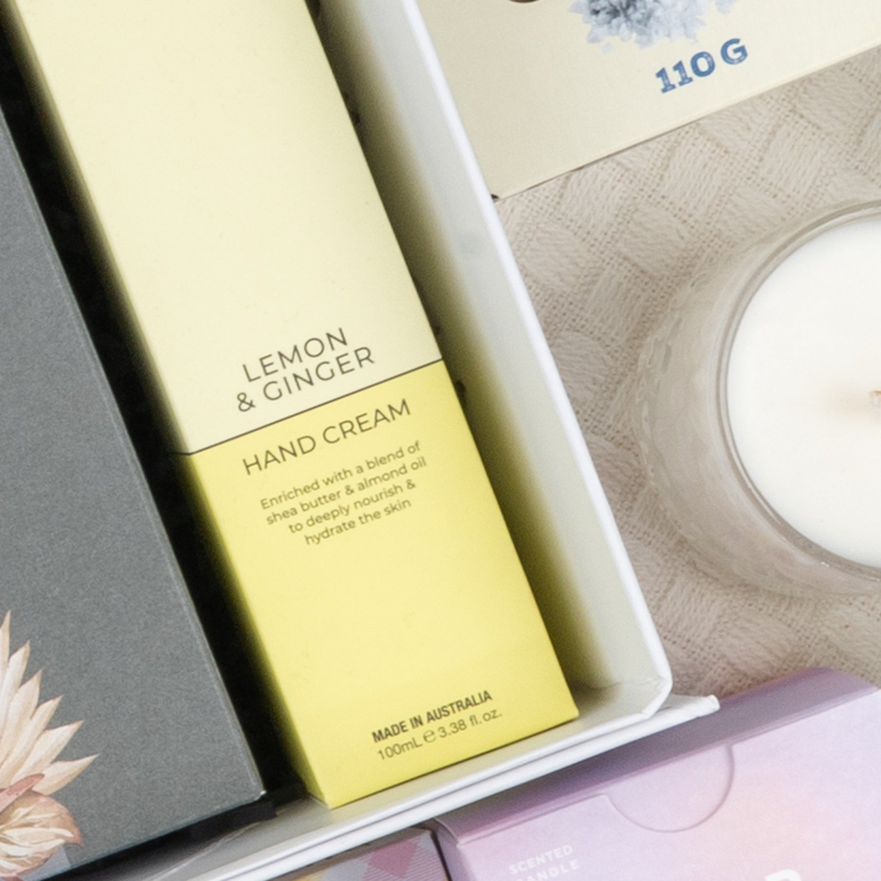 A close-up of the Ultimate Red Wine Celebration Hamper by The Hamper Boutique Co, featuring boxed items and a white candle arranged together in a gift box on a textured surface.