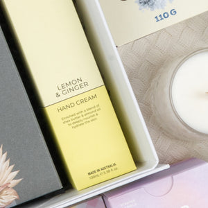 A close-up of the Ultimate Red Wine Celebration Hamper by The Hamper Boutique Co, featuring boxed items and a white candle arranged together in a gift box on a textured surface.