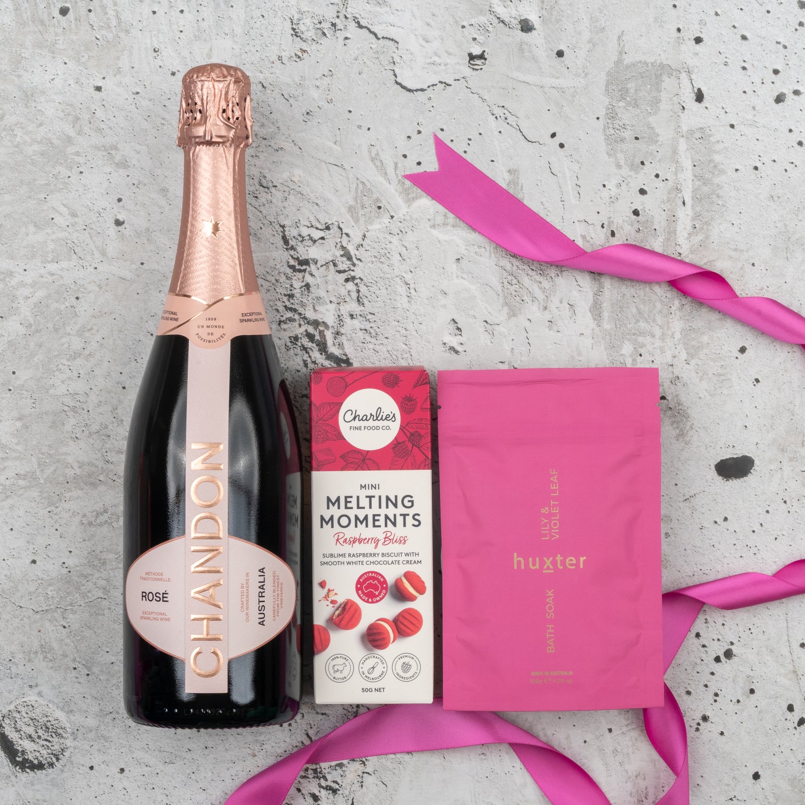 The Hamper Boutique Co’s Chandon Rosé Delights Hamper features Chandon Rosé, Charlies mini melting moments raspberry bliss, a pink Huxter soap bar, and a pink ribbon, all beautifully arranged on a light textured surface.