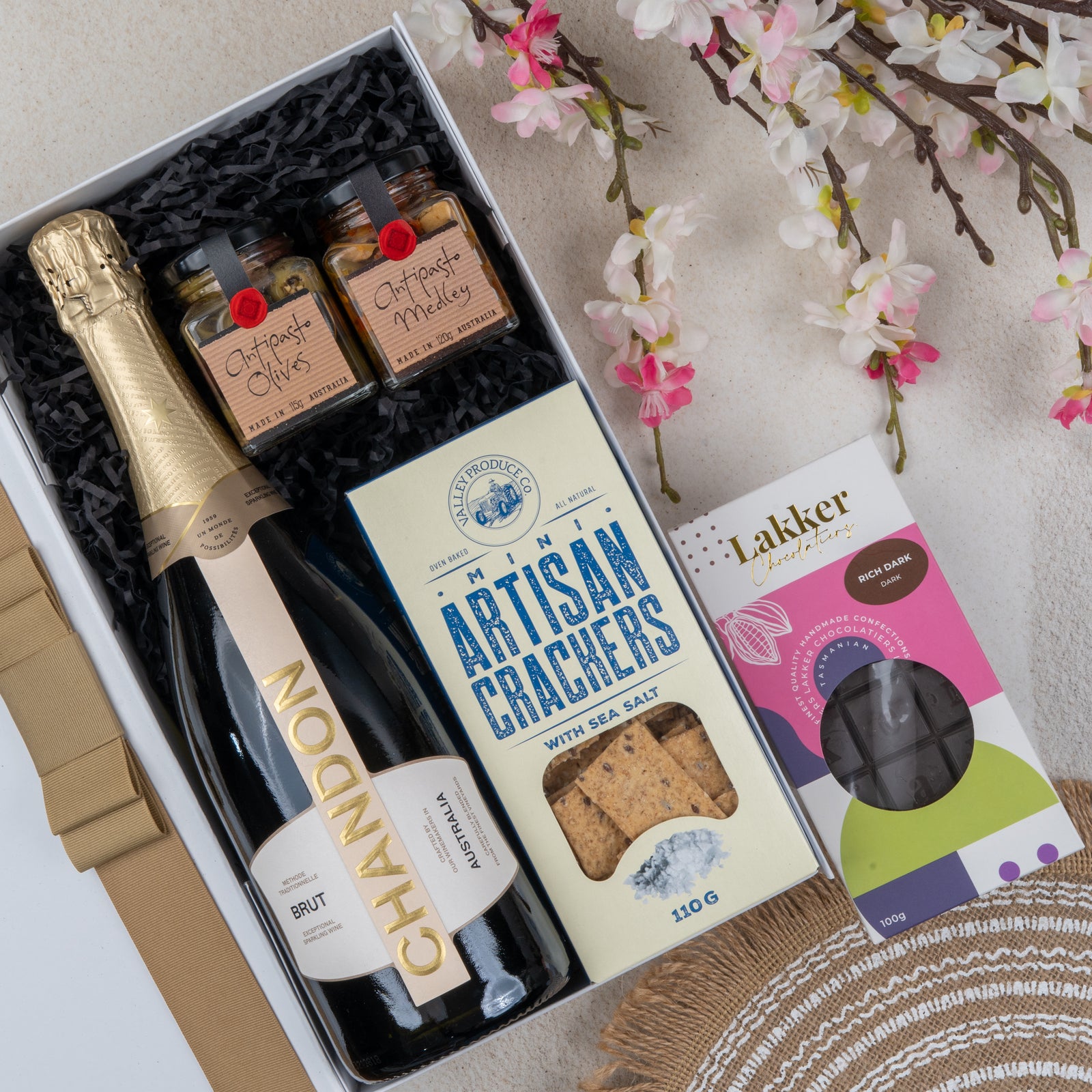 The Hamper Boutique Co’s Chandon Celebration Hamper features Chandon Brut, two antipasto jars (olives and medley), artisan crackers, Lakkar chocolates, plus flowers and a woven mat for an elegant gift presentation.