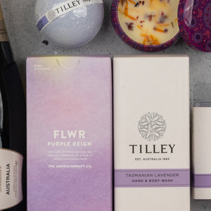 A close-up of The Hamper Boutique Co’s Chandon Deluxe Celebration Hamper featuring self-care items: a lavender bath bomb, floral candle, purple FLWR reed diffuser box, Tilley Tasmanian Lavender hand & body wash box, and a champagne bottle.