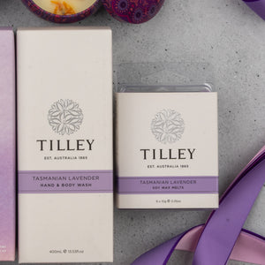 The Chandon Deluxe Celebration Hamper by The Hamper Boutique Co, presented in elegant white packaging with purple accents, is displayed on a gray surface with purple ribbon and decorative items nearby.