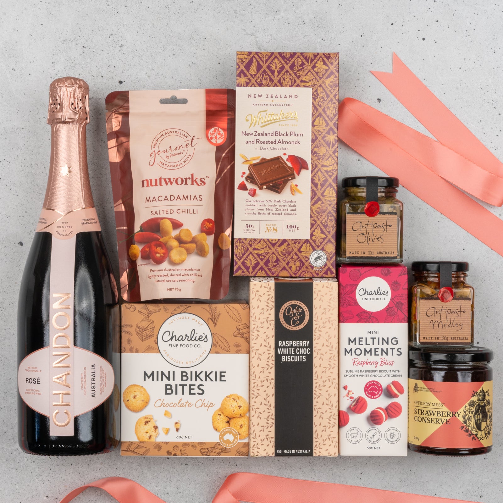 The Hamper Boutique Co's Chandon Rosé Deluxe Celebration Hamper includes Chandon rosé, salted chilli macadamias, raspberry biscuits, chocolate chip bites, plum & almond chocolates, raspberry preserve, strawberry conserve, and two gourmet relishes.