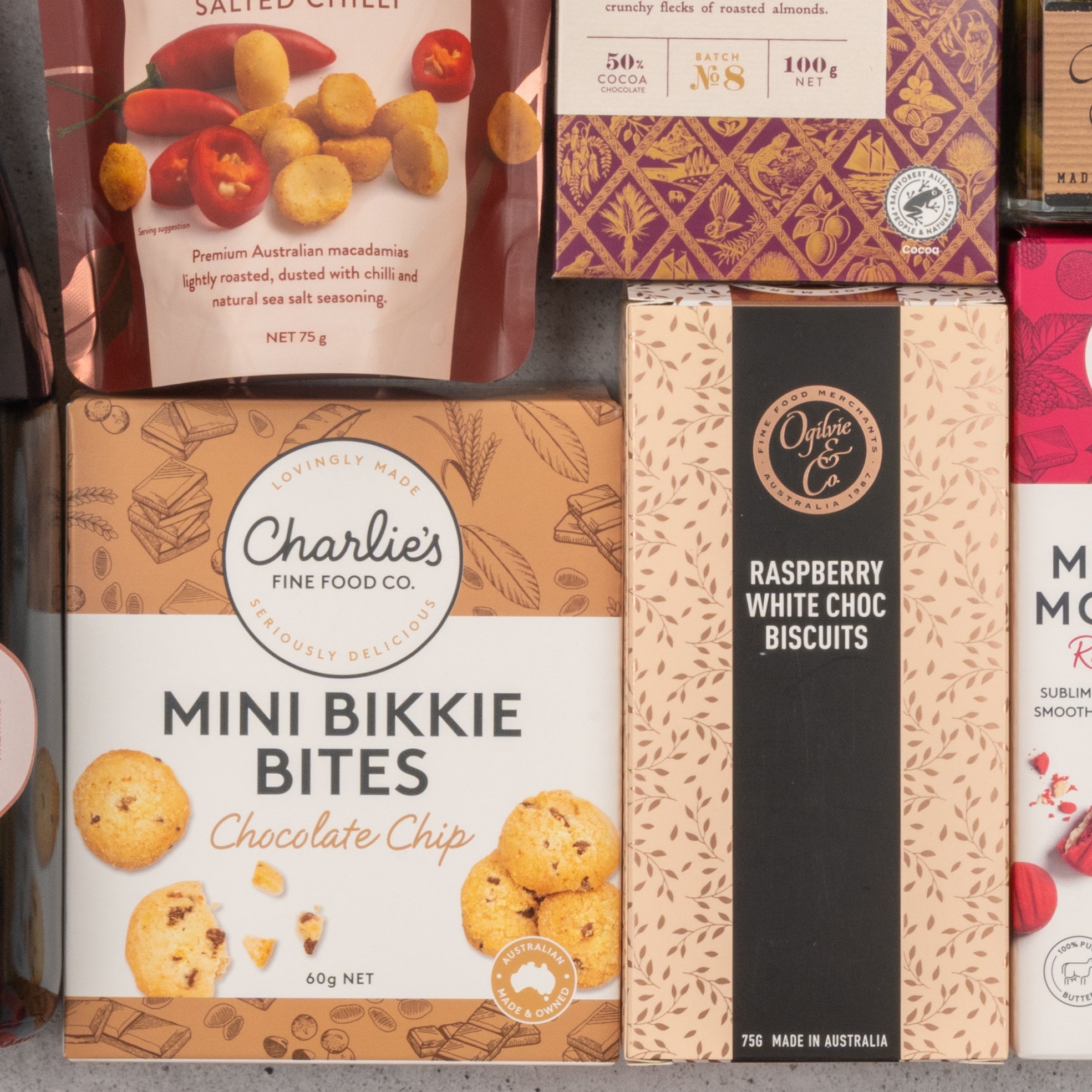 The Hamper Boutique Co’s Chandon Rosé Deluxe Celebration Hamper features a selection of snacks and biscuits, including chocolate chip mini bikkie bites and raspberry white choc biscuits, arranged together on a light surface.