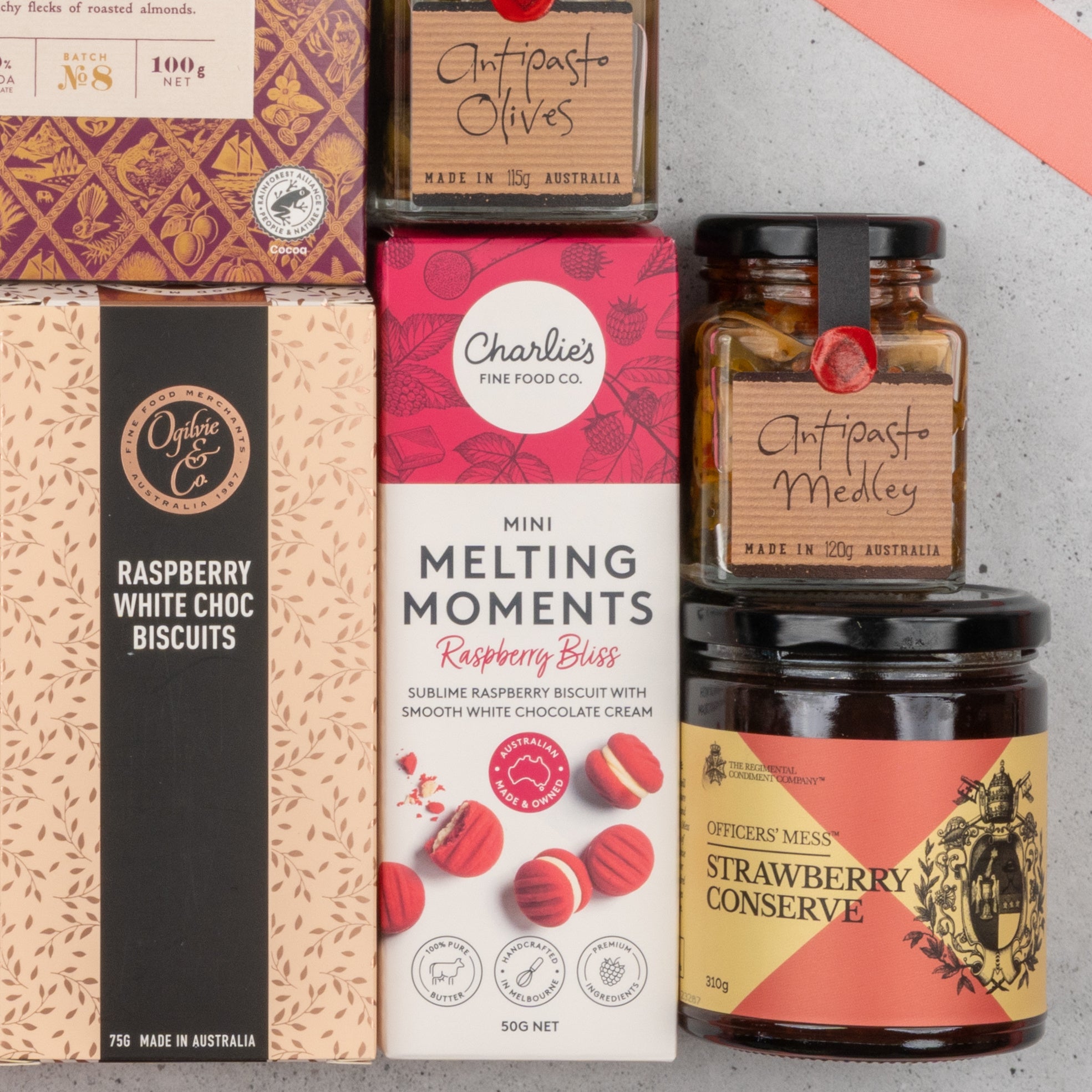 A close-up of The Hamper Boutique Co’s Chandon Rosé Deluxe Celebration Hamper, featuring raspberry biscuits, mini melting moments, olives, antipasto medley, and strawberry conserve in vibrant boxes and jars, arranged neatly together.