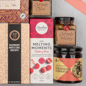 A close-up of The Hamper Boutique Co’s Chandon Rosé Deluxe Celebration Hamper, featuring raspberry biscuits, mini melting moments, olives, antipasto medley, and strawberry conserve in vibrant boxes and jars, arranged neatly together.