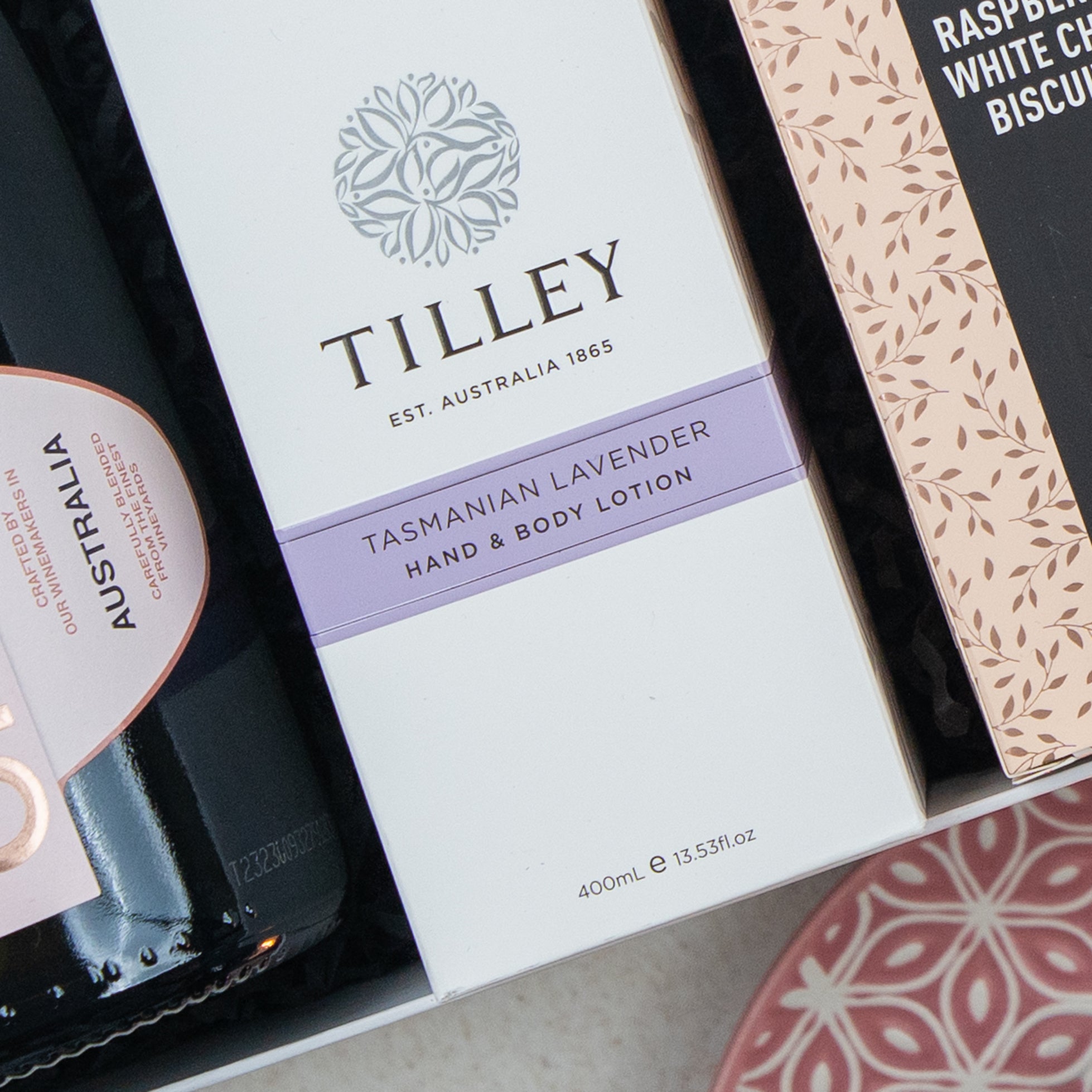 A close-up of The Hamper Boutique Co Chandon Rosé Luxury Selection Hamper next to a dark bottle labeled “Australia” and a package of raspberry and white chocolate biscuits.