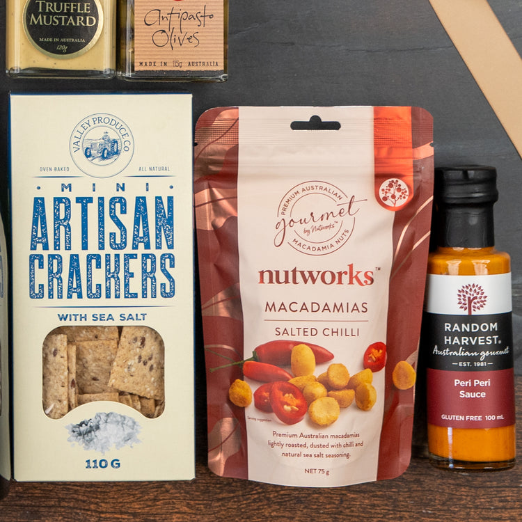 The Moët & Chandon Celebration Hamper by The Hamper Boutique Co includes mini artisan crackers, salted chili macadamias, peri peri sauce, truffle mustard, and antipasto olives displayed on a wooden surface.