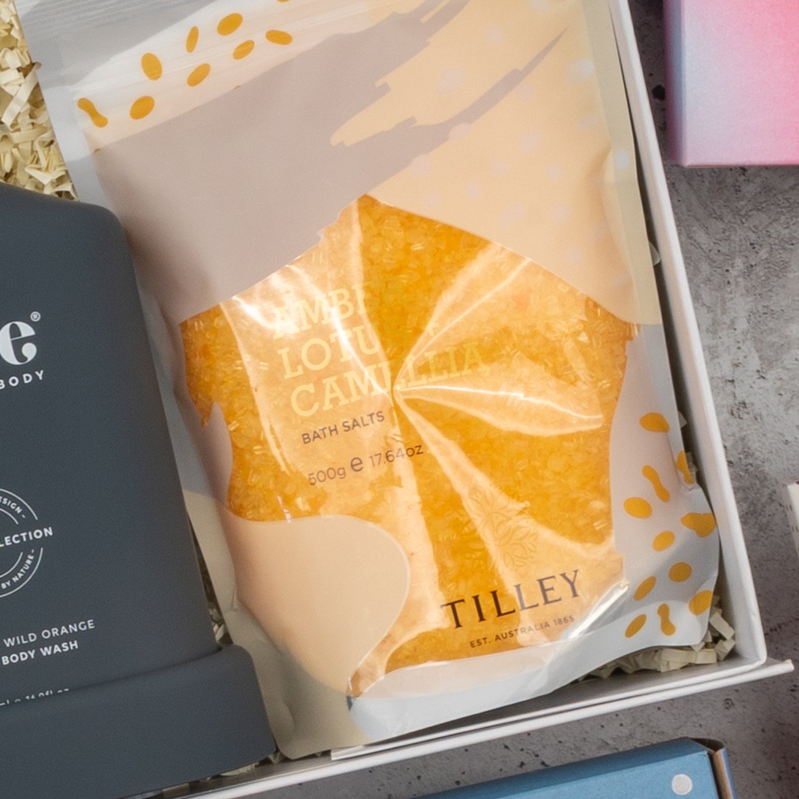 A package of Champagne Wellness Escape bath salts from The Hamper Boutique Co is displayed in a gift box, surrounded by shredded paper and other bath products.