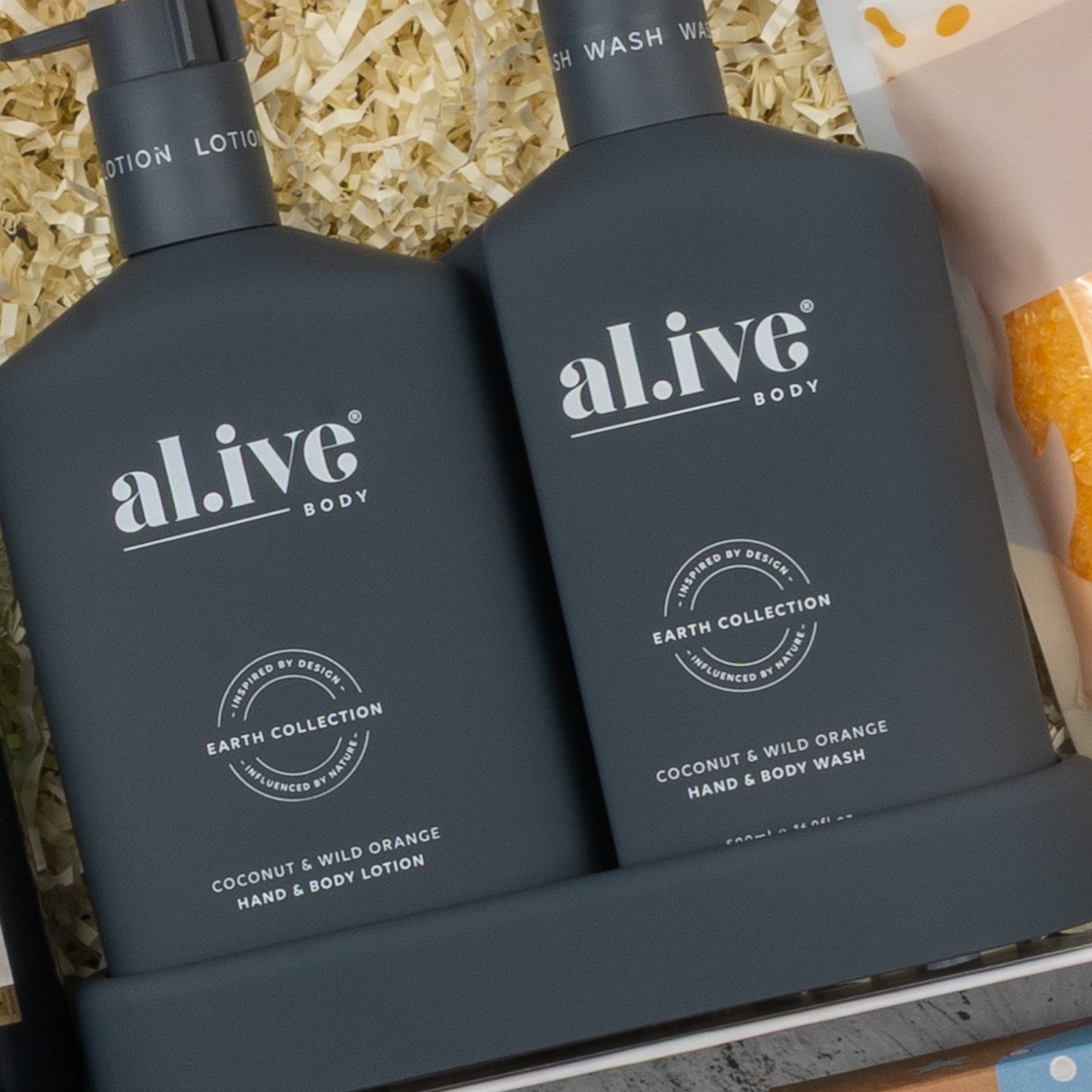 Two dark gray bottles of The Hamper Boutique Co Champagne Wellness Escape hand and body lotion and body wash in a tray, displayed on shredded paper packaging.