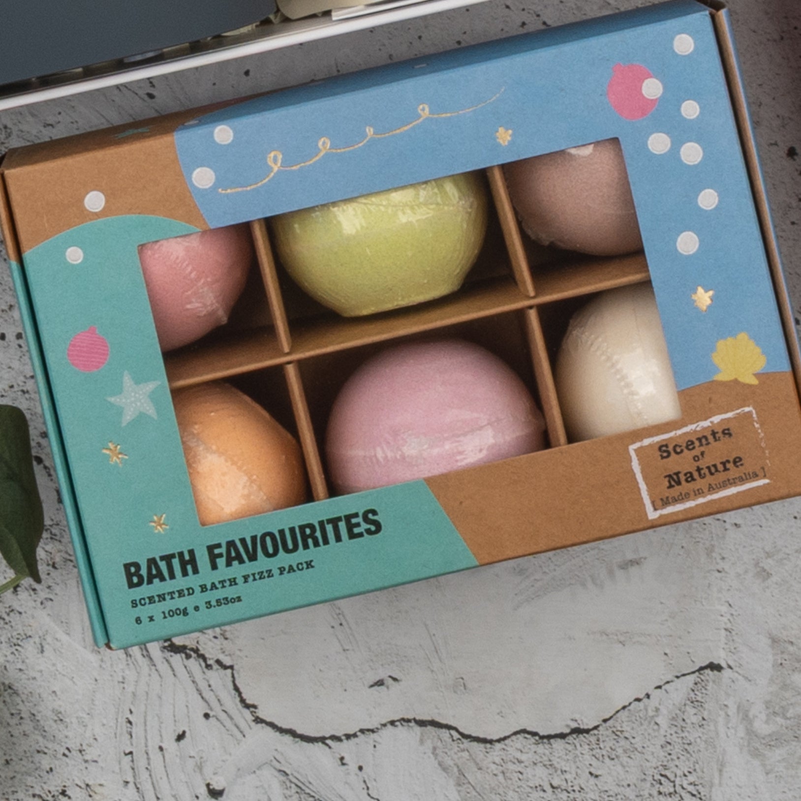 A box of six colorful bath bombs labeled Champagne Wellness Escape with a window displaying the bath bombs inside. The packaging features teal, brown, and white designs and is branded as The Hamper Boutique Co.