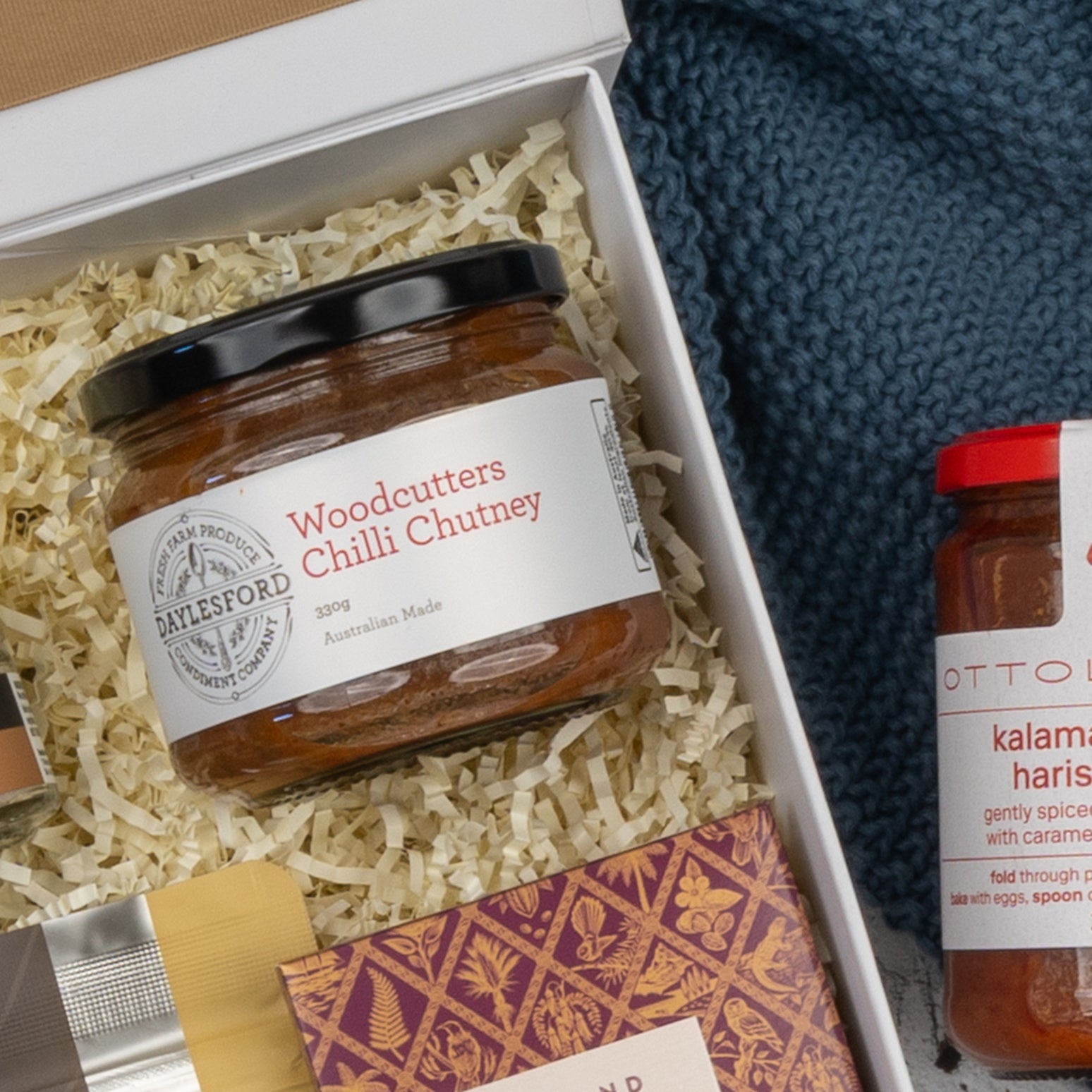 A close-up of The Hamper Boutique Co’s Moët & Chandon Premium Celebration Hamper shows a gift box with shredded paper, a partially visible patterned box, and a blue knitted item.