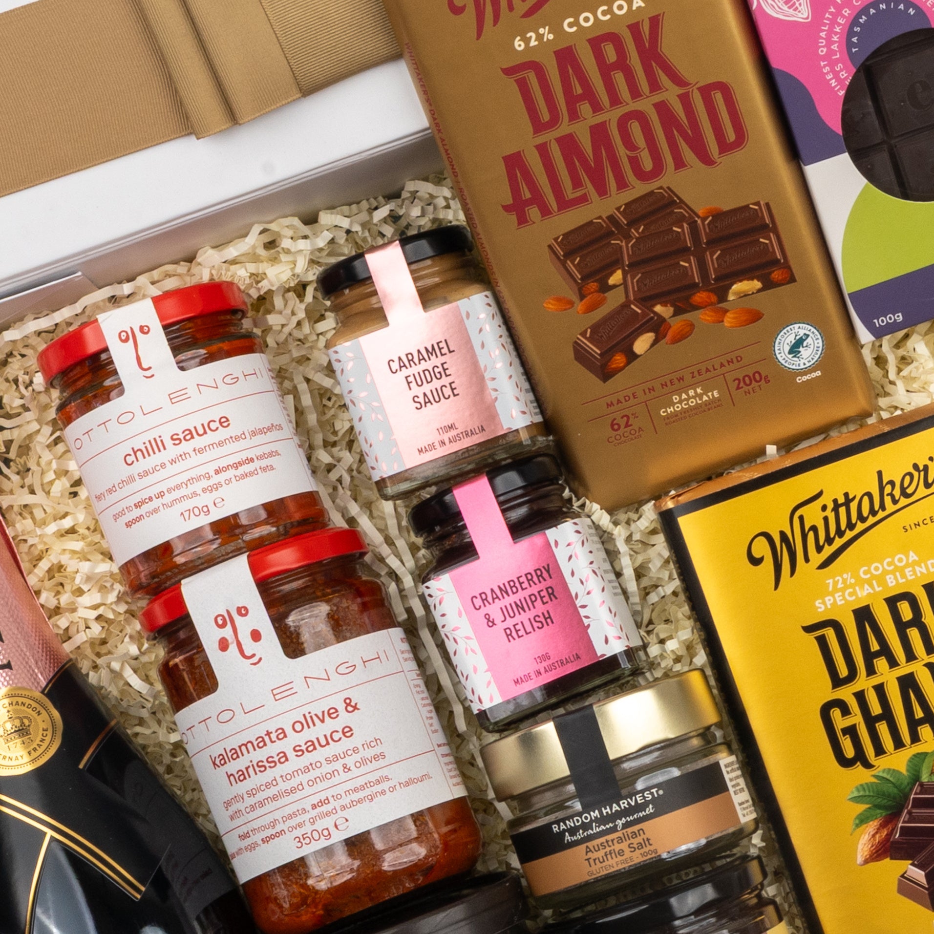 The Hamper Boutique Co Moët & Chandon Rosé Grand Celebration Hamper includes chilli sauce, kalamata olive & harissa sauce, cranberry juniper relish, caramel fudge, dark chocolate bars, and wine in a bed of shredded paper.